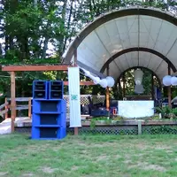 Outdoor forest bandshell with tall blue speaker stacks on both sides of the stage