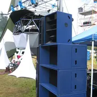 Tall stack of blue speaker cabinets beside a lighting truss and white tent