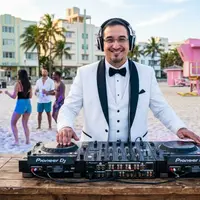 DJ in a white tuxedo jacket at a controller on a table on a beach
