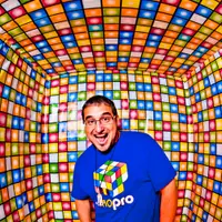 Full-length fisheye photo of MontsDe in a blue Mo'Pro cube-logo shirt in a room tiled with colorful squares