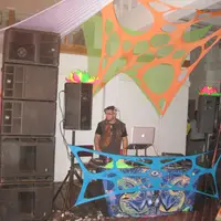 DJ booth set between tall speaker stacks in a room hung with orange and blue fabric art