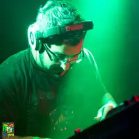 DJ in glasses and headphones lit in green over the mixer