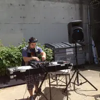 DJ set up outdoors on a small table with a speaker on a stand beside a concrete wall