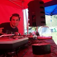 DJ behind turntables under a red tent with a speaker overhead