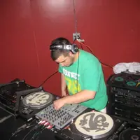 DJ mixing on turntables and a club mixer in a red-walled room