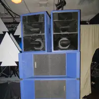 Four-high stack of blue speaker cabinets on a dance floor in front of white triangle decor