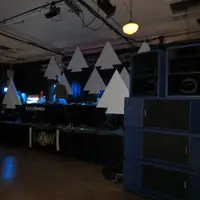 Dim ballroom with a speaker stack on the right and white triangle decor above a stage