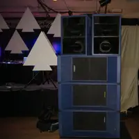 Blue speaker stack and white paper-cut triangles in a ballroom before a show