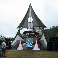 Peaked tent stage in a forested valley with speaker stacks beside it