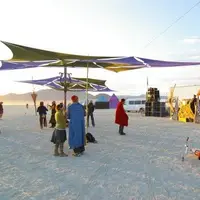 Wide desert scene with shade structures, a yellow structure and speaker stacks