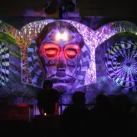 Psychedelic outdoor stage with a glowing face sculpture between two lit circular panels