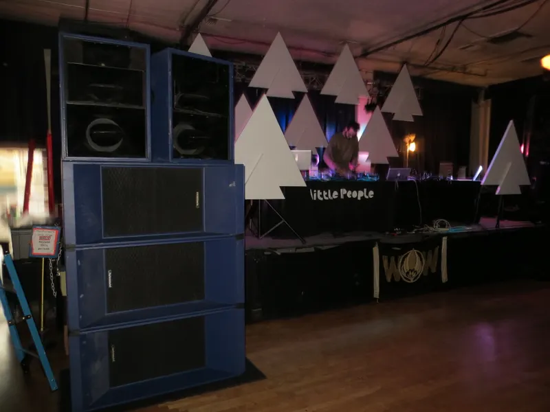 Stacked blue speaker cabinets beside a DJ table in a dim hall before a show