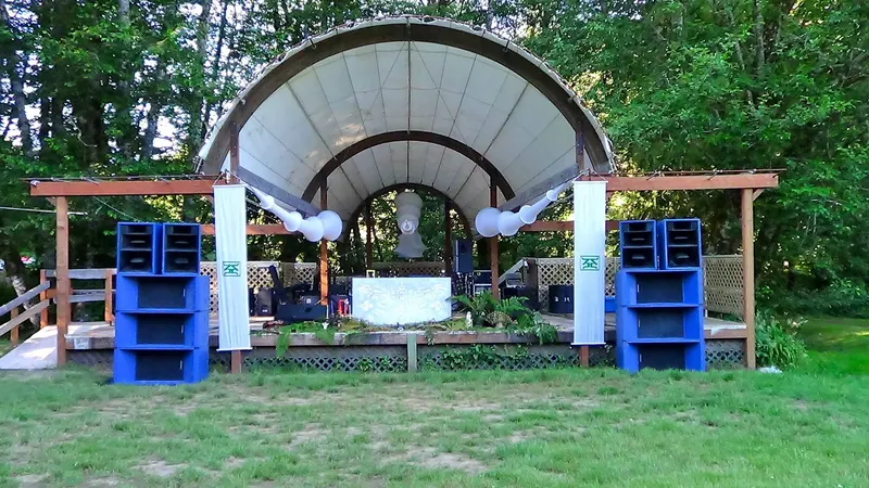 Outdoor forest bandshell stage with a tall stack of blue speaker cabinets on each side