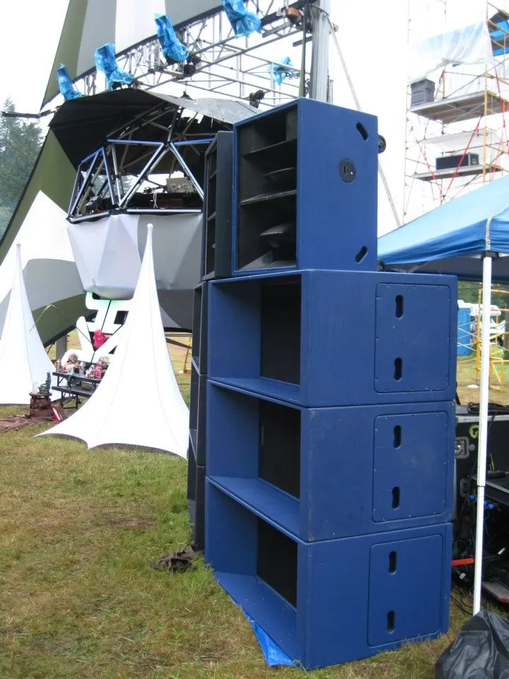 Tall stack of blue speaker cabinets beside a lighting truss and white tent