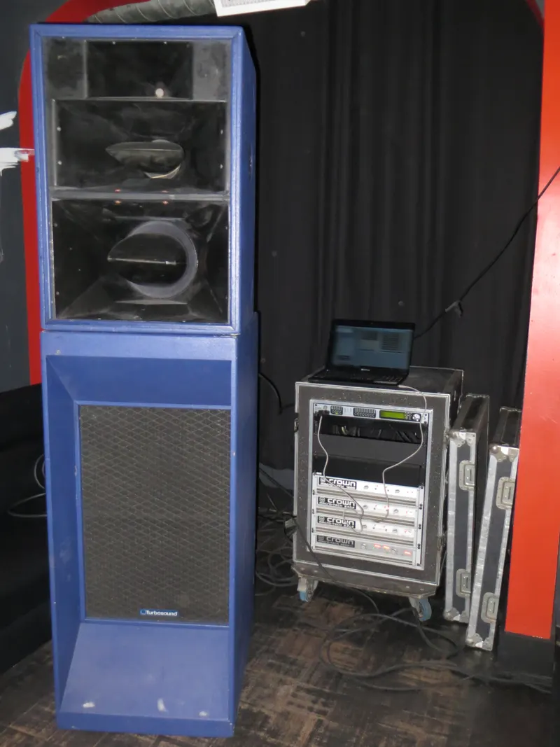 Tall blue speaker stack next to an amplifier rack case and a monitor backstage